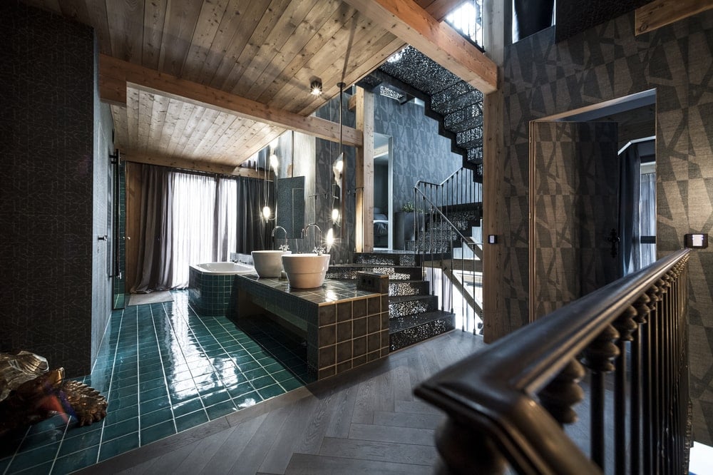On the side of the intricate staircase is the large bathroom with green tiles and large freestanding sinks.