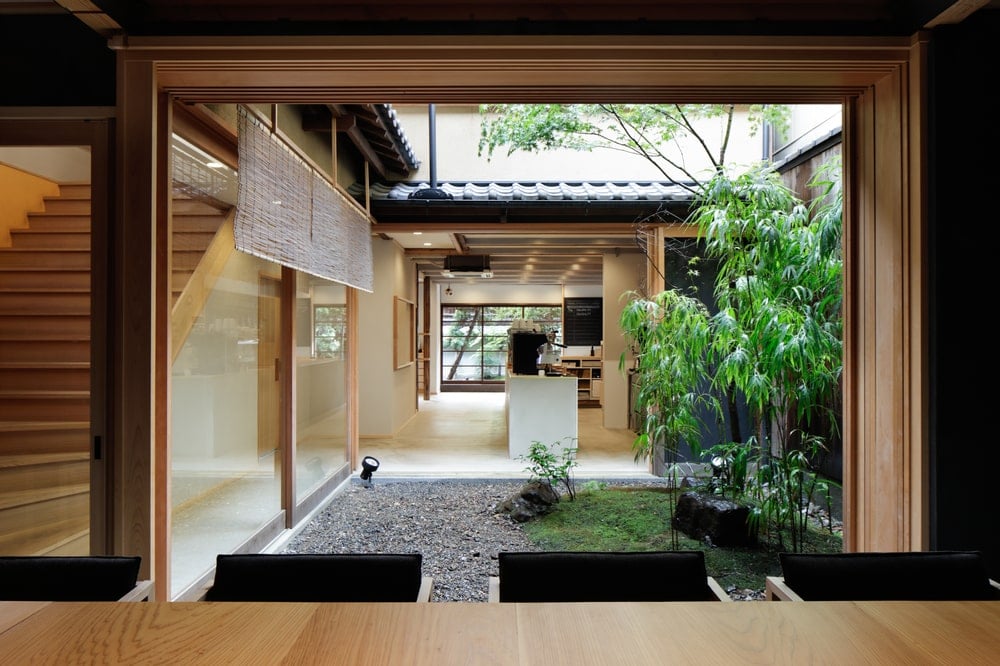 Behind the wooden stools of the bar is a zen garden with graveled walkways and trees.