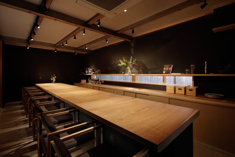 This is a close look at the bar with a large wooden counter paired with wooden stools and a tall wooden ceiling with modern lighting.