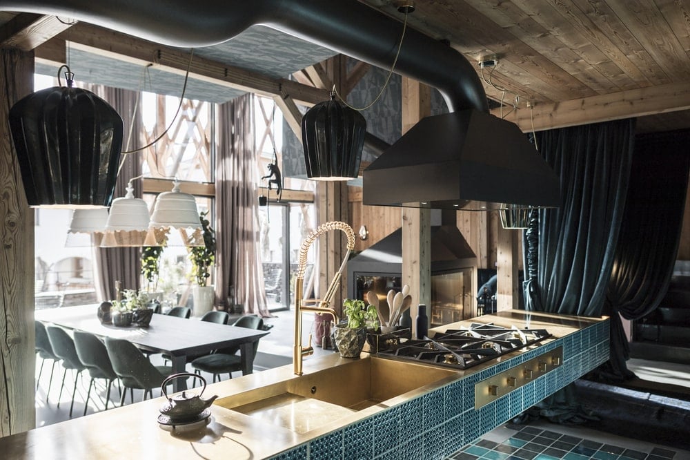 This is a close look at the cooking area with sea green tiles that make the black elements of the stove and vent hood stand out.