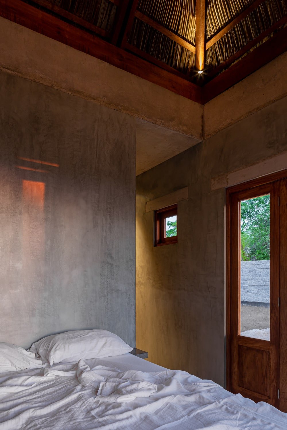 This is a close look at the bedroom that has a white bed cushion that stands out against the concrete structures.