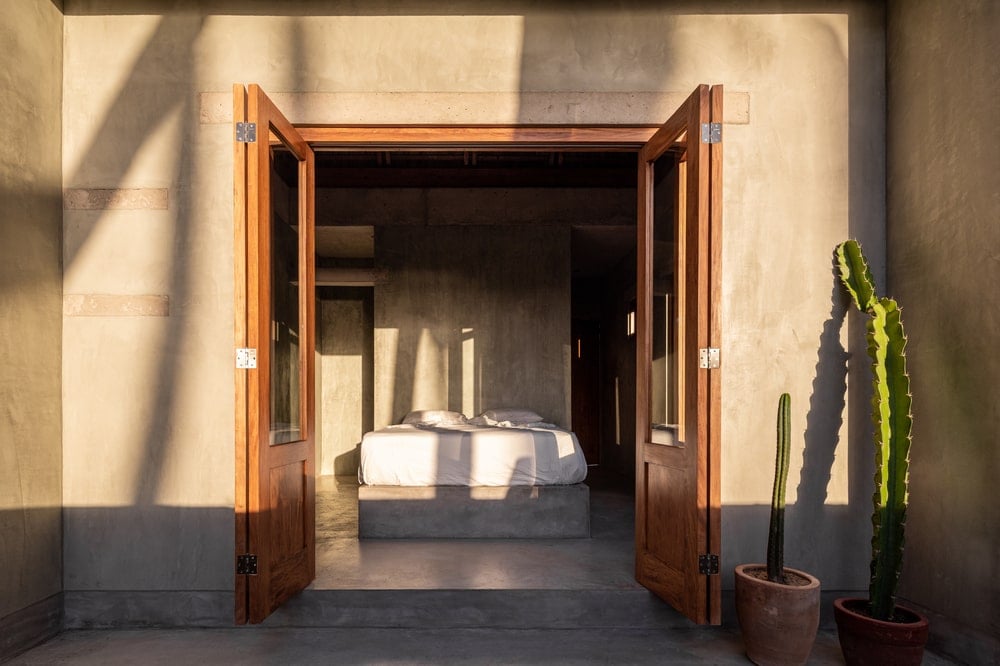 This is exterior view of the section of the house looking into the bedroom with concrete walls, wooden doors and cacti on the side.