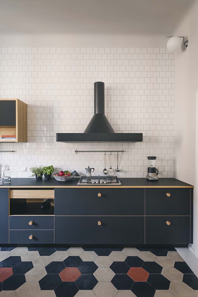 This is a look at the structure of the kitchen that has dark drawers and a dark vent hood that stands out against the white subway tiles.