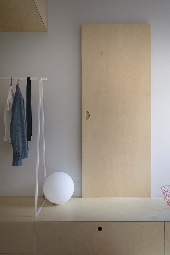 This is a close look at the low wooden structure on the side of the bed with a door decoration, a spherical light and a clothes rack.