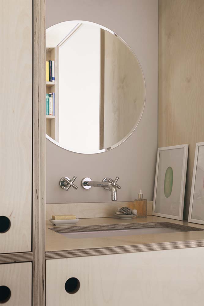 This is a close look at the sink of the bathroom housed in a large wooden structure topped with a round mirror.