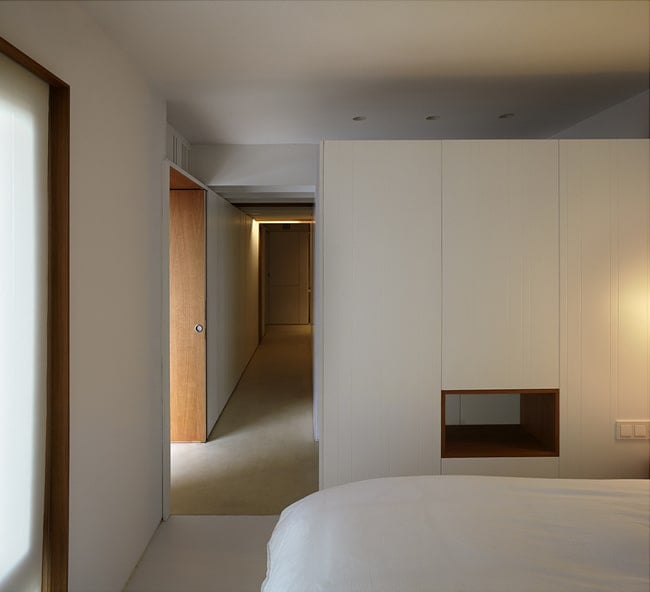 On the other side of this long hallway is the bedroom with white walls and ceiling.