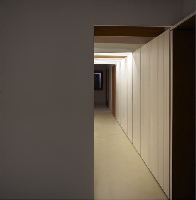 This is another look at the long and narrow hallway of the house with warm lighting and white walls.