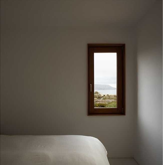 On the other wall of the bedroom is a small rectangular window that shows a view of the outdoors and lets in natural lighting.