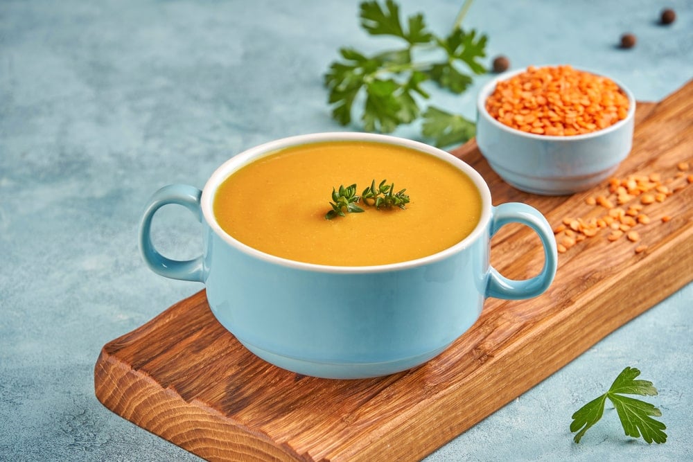 A bowl of red lentil soup on a wooden board.