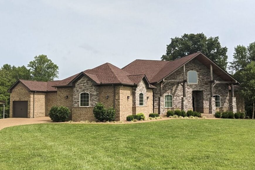 Front exterior view showing the stone cladding, rustic trims, arched windows, and angled garage.