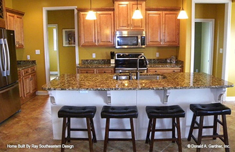 Kitchen with wooden cabinetry, stainless steel appliances, granite countertops, and a breakfast island fitted with a double bowl sink.