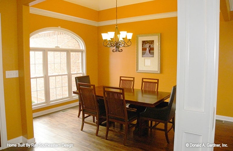 The formal dining room offers a wooden dining set, a classic chandelier, and a large arched window that brings natural light in.