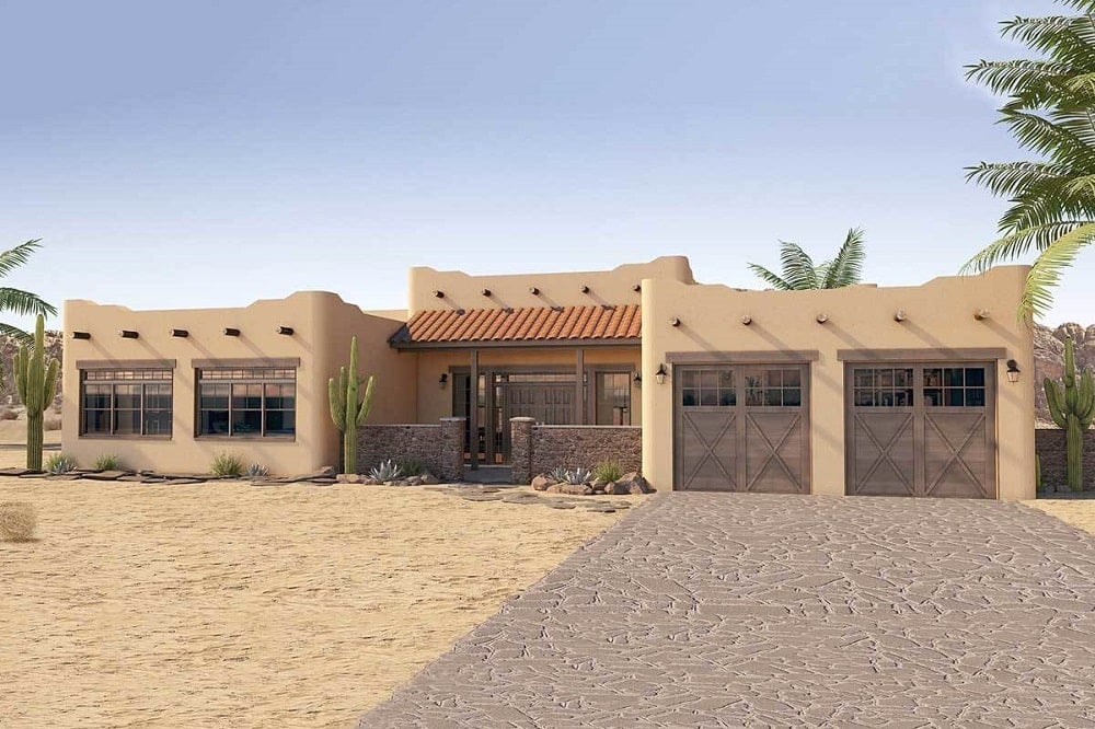 This is a look at the single story adobe house with an earthy beige tone to its exterior walls complemented by the exposed wooden beams and mosaic stone driveway.