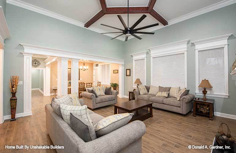 The living room has gray seats, dark wood tables, and three framed windows covered in white blinds.