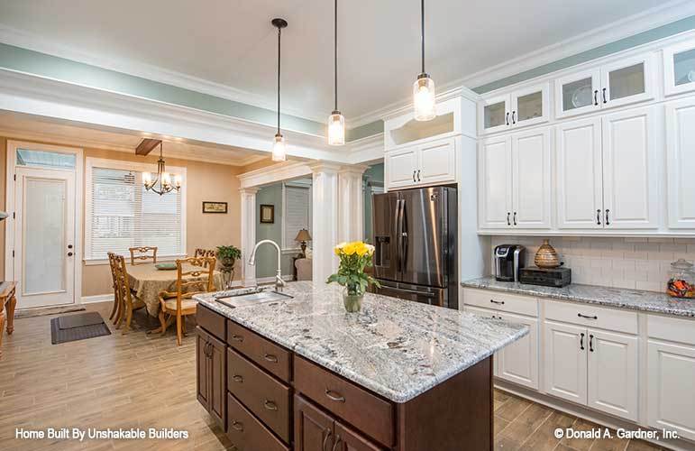 The kitchen is equipped with stainless steel appliances, white cabinetry, granite countertops, and a prep island fitted with a sink.