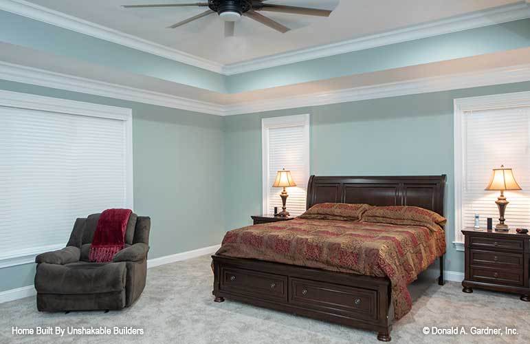 Primary bedroom with carpet flooring, muted green walls, and a tray ceiling mounted with a fan.