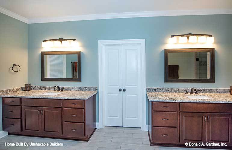 The primary bathroom features his and her vanities flanking a white double door that opens to the walk-in closet.