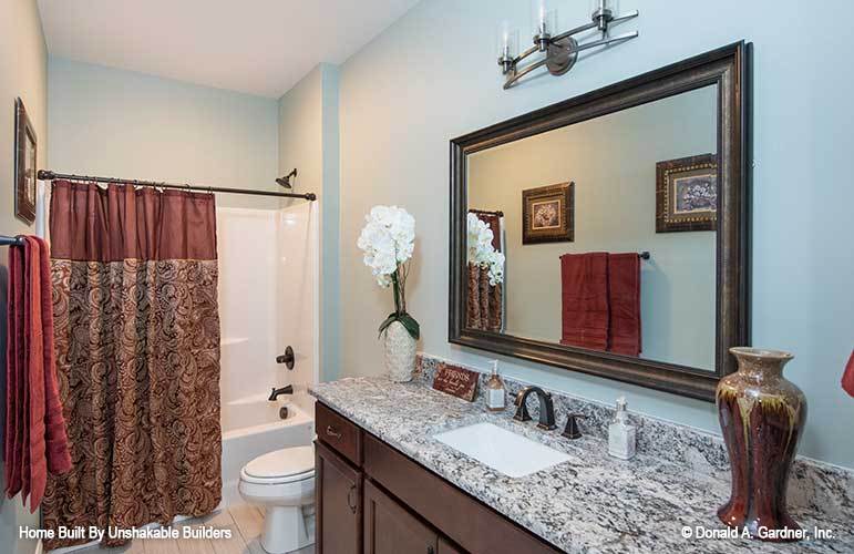 Bathroom with a sink vanity, a toilet, and a tub and shower combo enclosed in a patterned curtain.