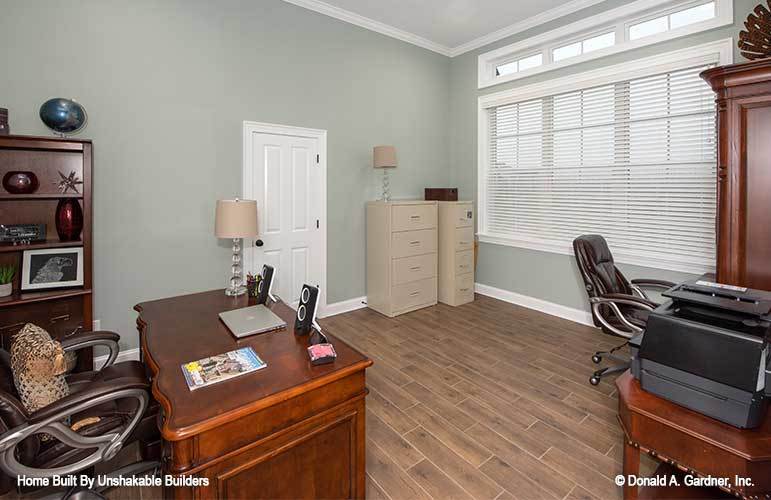 Study with wooden furnishings, leather swivel chairs, and three-paneled windows allowing natural light in.