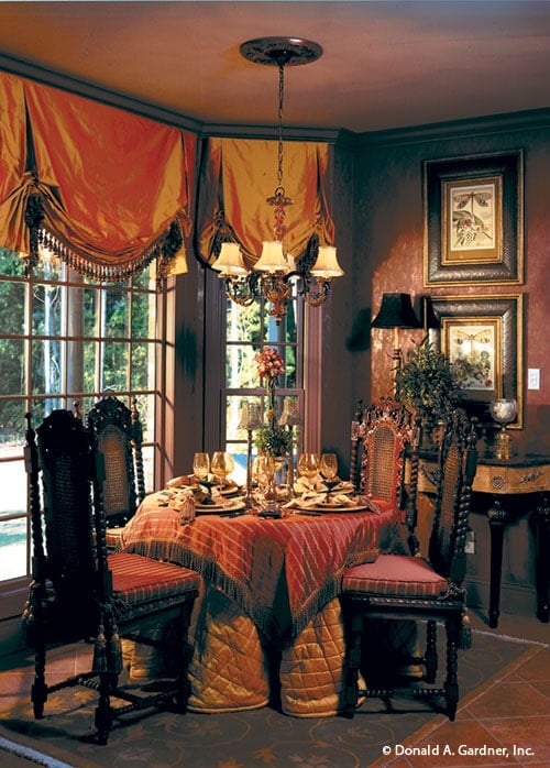 Breakfast nook with a round dining set, a warm chandelier, and a bay window dressed in classy roman shades.