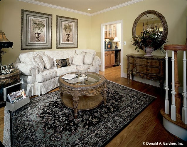 The sitting room has skitted sofa, a glass top coffee table, and yellow walls adorned with framed artworks.