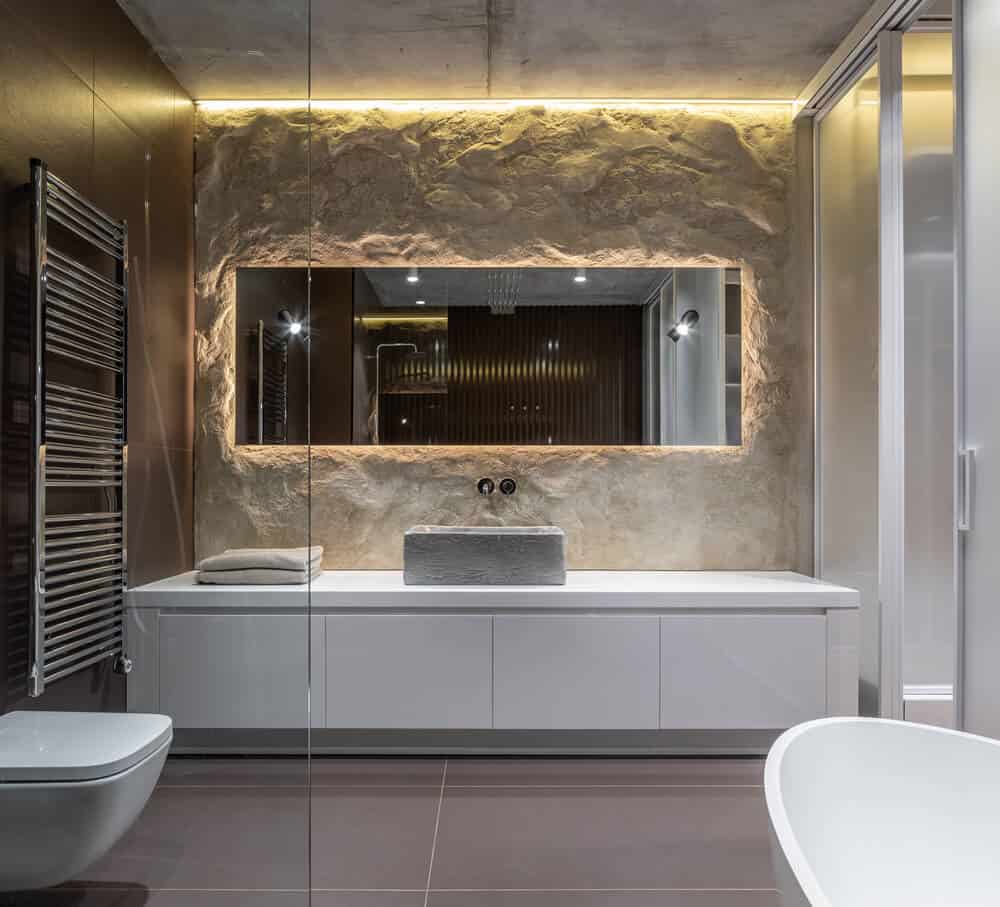 This is a look at the primary bathroom that has gray flooring tiles to contrast the white vanity, white toilet and white freestanding bathtub on the other side.
