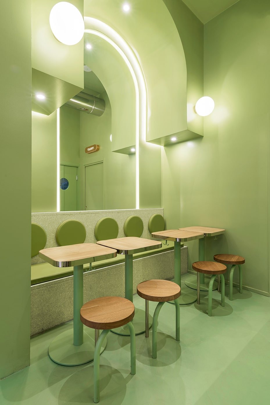 This is a close look at the far green corner of the restaurant with consistent green walls, floor, ceiling and structures complemented by the wooden tables, chairs and the large mirror.