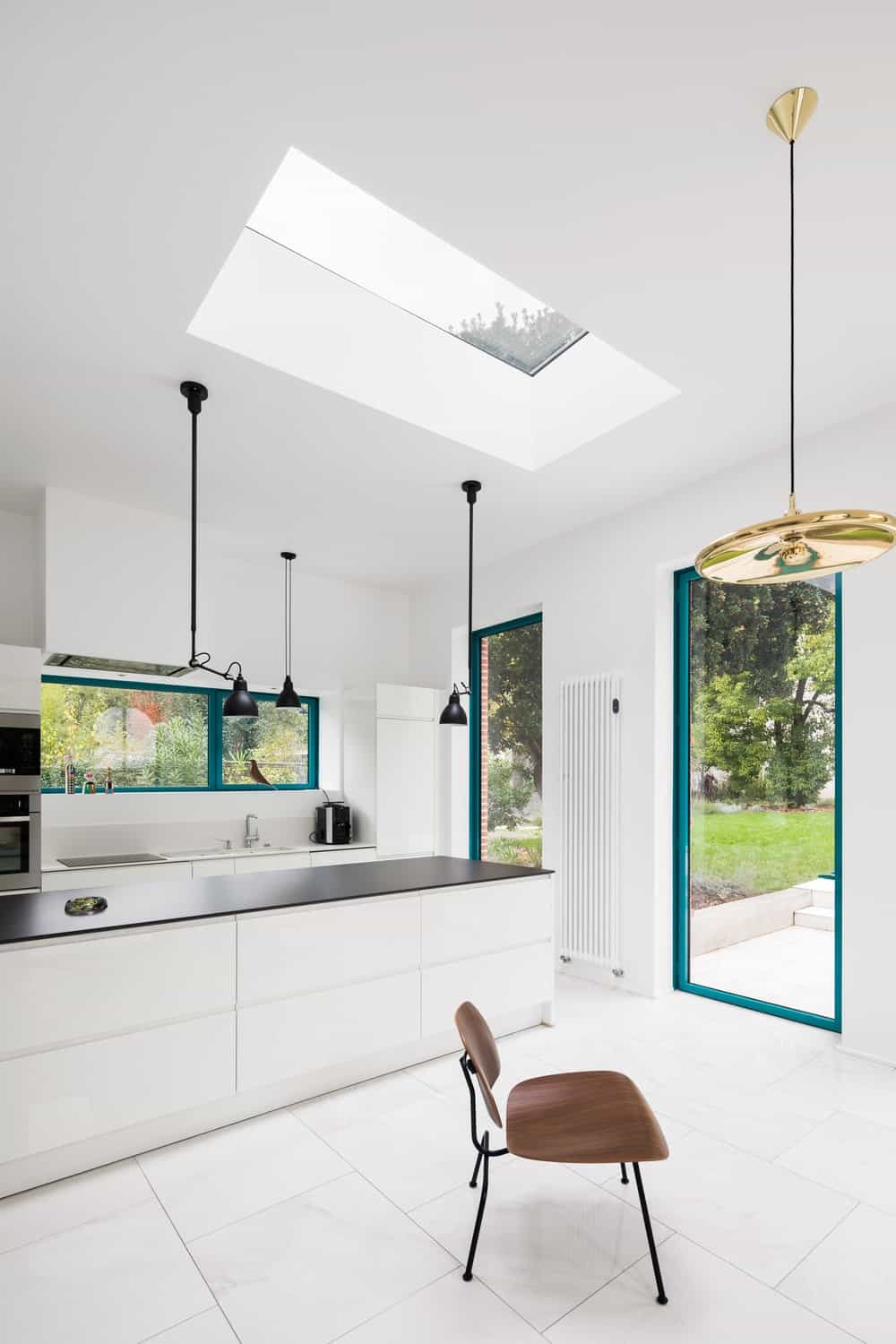 This is a simple and bright minimalist kitchen with a white ceiling and a skylight that brightenes the large white kitchen island topped with a black countertop.