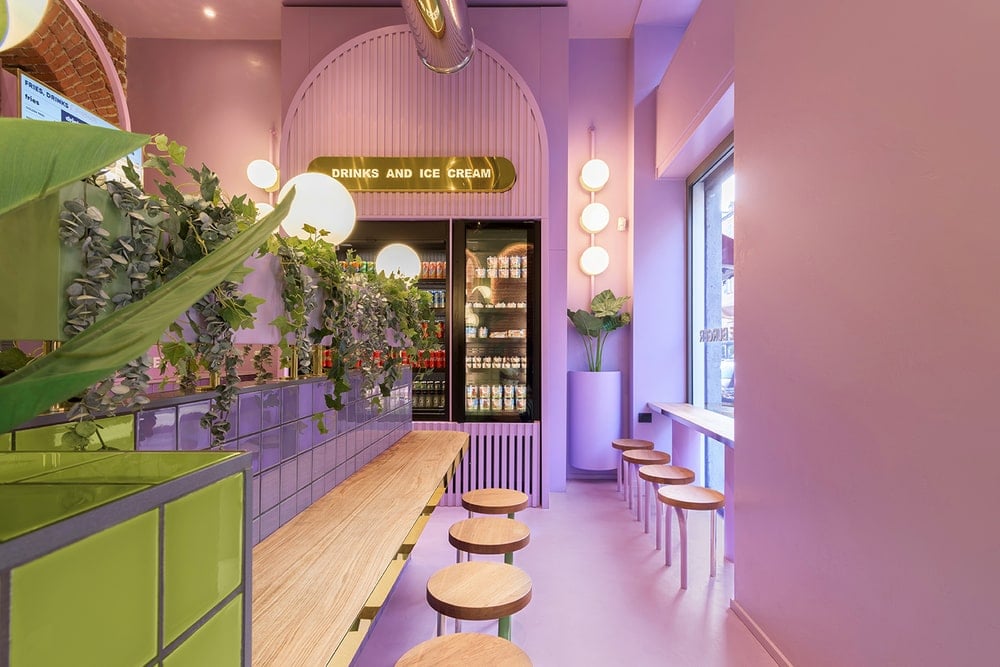 This is a side of the restaurant with bar stools and built-in wooden bars complemented by the purple tone of the floor, walls and ceiling adorned with vines and warm lighting.