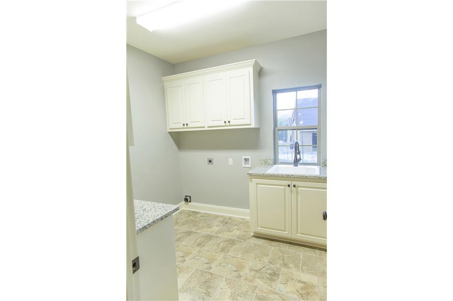 Laundry room with white cabinets, granite countertops, and a porcelain sink placed under the window.