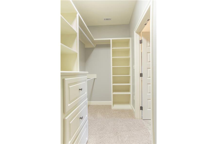 Primary walk-in closet with carpet flooring and white built-in shelves.