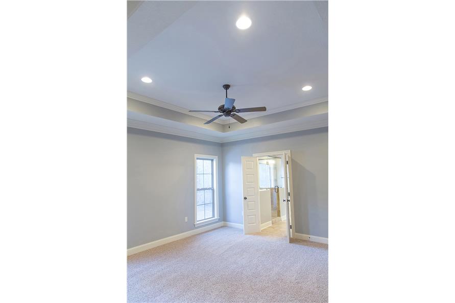 Primary bedroom with carpet flooring and a tray ceiling mounted with a fan and recessed lights.