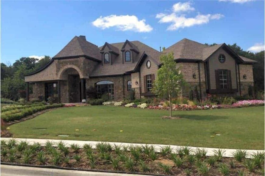 Front-right exterior view showing the serene landscaping with colorful flowers bordering the angled garage.