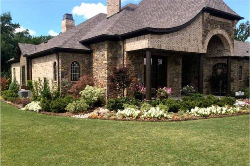 Front-left exterior view with brick chimneys, hipped rooflines, and verdant landscaping.