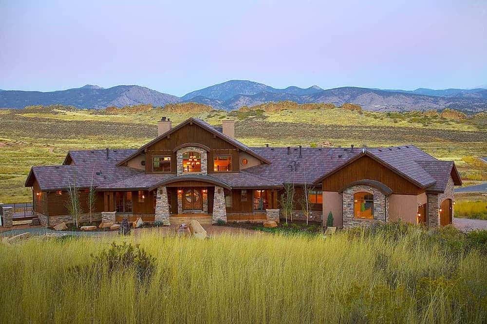 This is an exterior view of the mountain chalet-style home with dark wooden exterior walls complemented by the landscaping of shrubs, decorative rocks and stone mosaic accents.