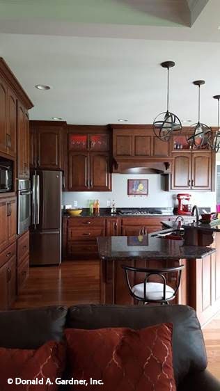 The kitchen offers wooden cabinetry, black granite countertops, and a raised peninsula attached with an eating bar.