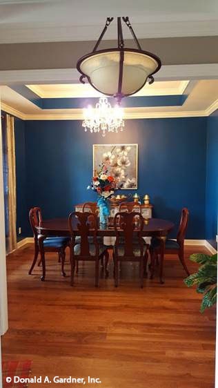 The formal dining room has blue walls, wooden furnishings, and a stunning tray ceiling adorned with a beaded chandelier.