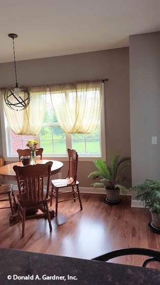Breakfast nook with a round dining set, a spherical chandelier, and three-paneled windows dressed in sheer valances.