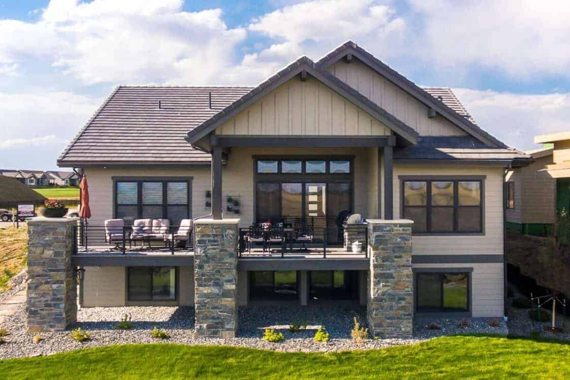 This is a look at the back of the house that is supported with large stone mosaic pillars that go well with the landscaping of graveled soil, shrubs and grass lawn.