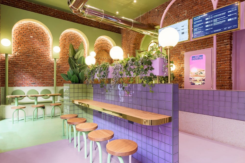 This is a close look at a space-saving divider of the restaurant with green and purple tiles on it and has a built-in bar paired with stools.