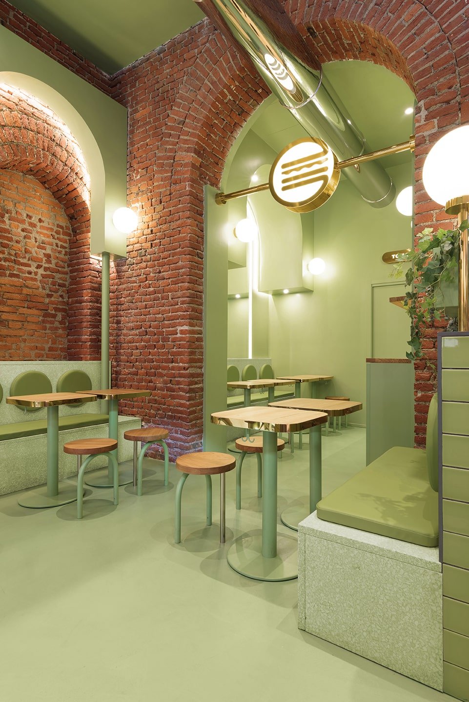 This is a close look at the green edge of the restaurant with its tall archway, red brick wals and contrasting green tone on its floor, wall and ceiling that has exposed vents.