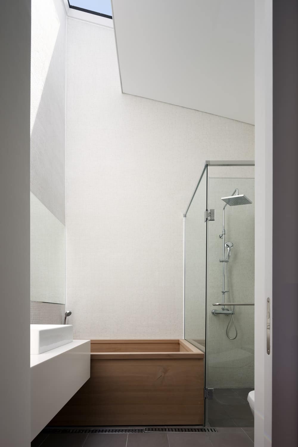 This is a close look at the primary bathroom with a tall arched ceiling, white walls, a glass-enclosed shower area and a wooden bathtub by the white sink.