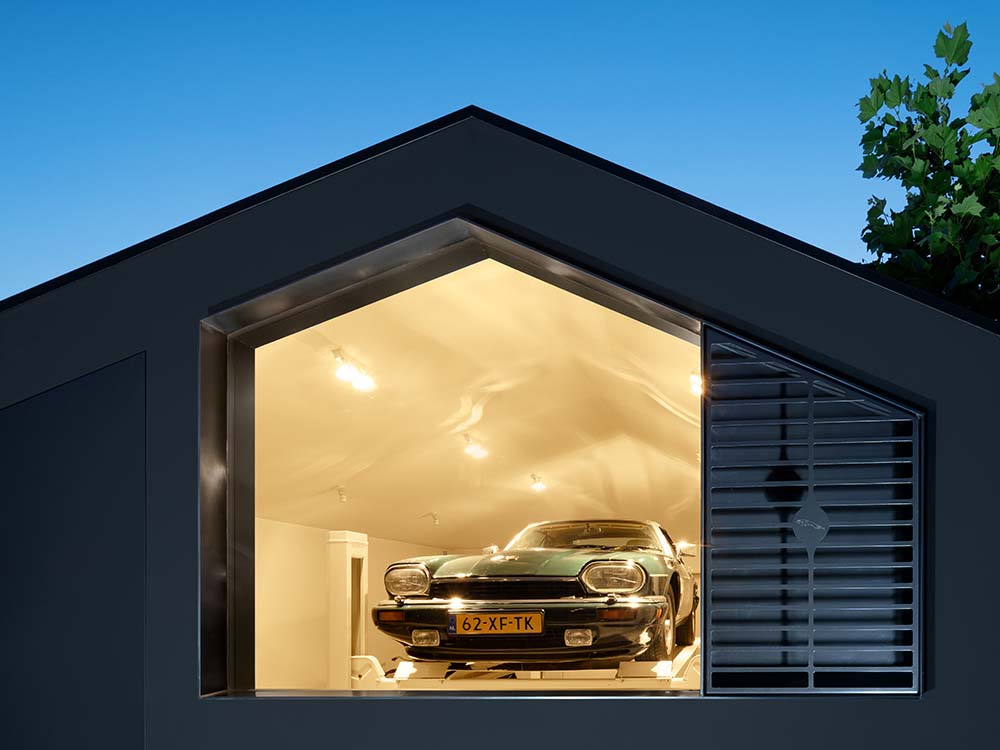 This is a nighttime view of the garage that has a warm yellow from its interior lights escaping through the glass wall.