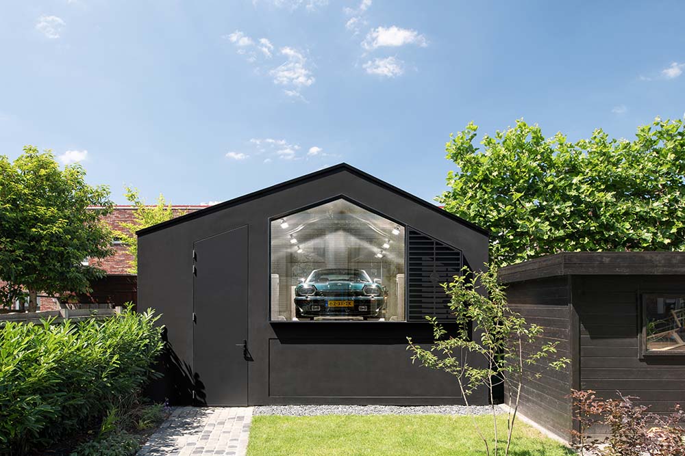 This is a view of the garage adorned with a grass lawn and a concrete walkway lined with shrubs on the side.