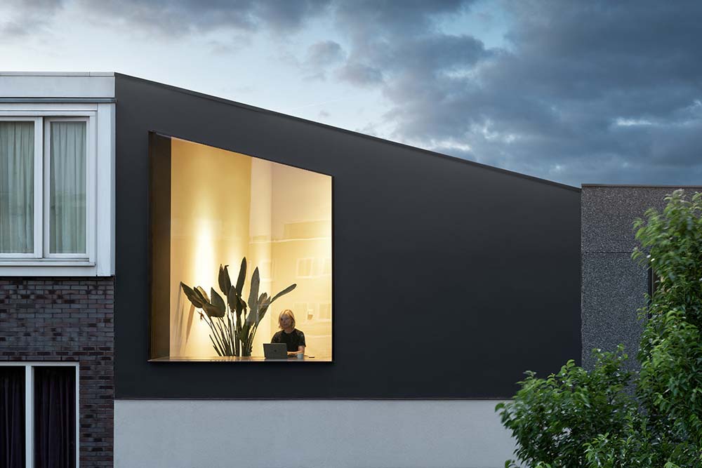 This is a nighttime view of the house showcasing the warm glow of the glass window that pairs well with the dark gray exterior.