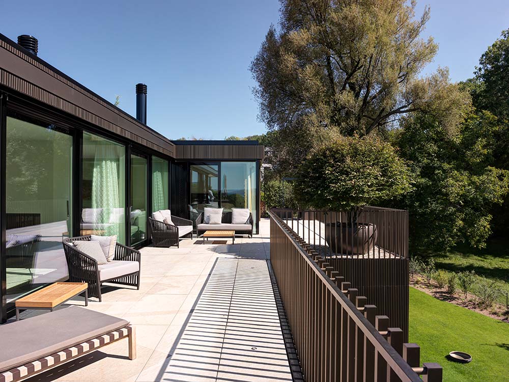 This is a close look at the house's terrace balcony with dark brown metal railings to match the dark brown exterior walls fitted with various lounge areas.