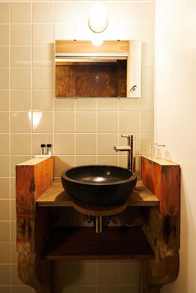 The wooden vanity has a dark bowl sink paired with a stainless steel faucet and a wall mounted mirror.