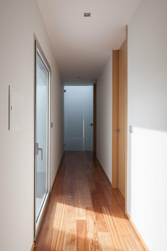 This is an upper floor hallway with bright beige walls and ceiling complemented by the hardwood flooring. There is also a glass door on the side.