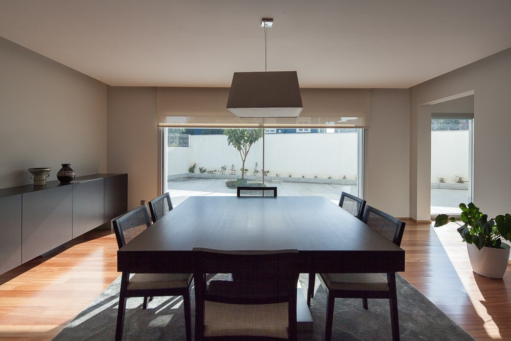 This is a close look at the dining room of the house with a large dark wooden dining table surrounded by wooden chairs and topped with a decorative lighting.