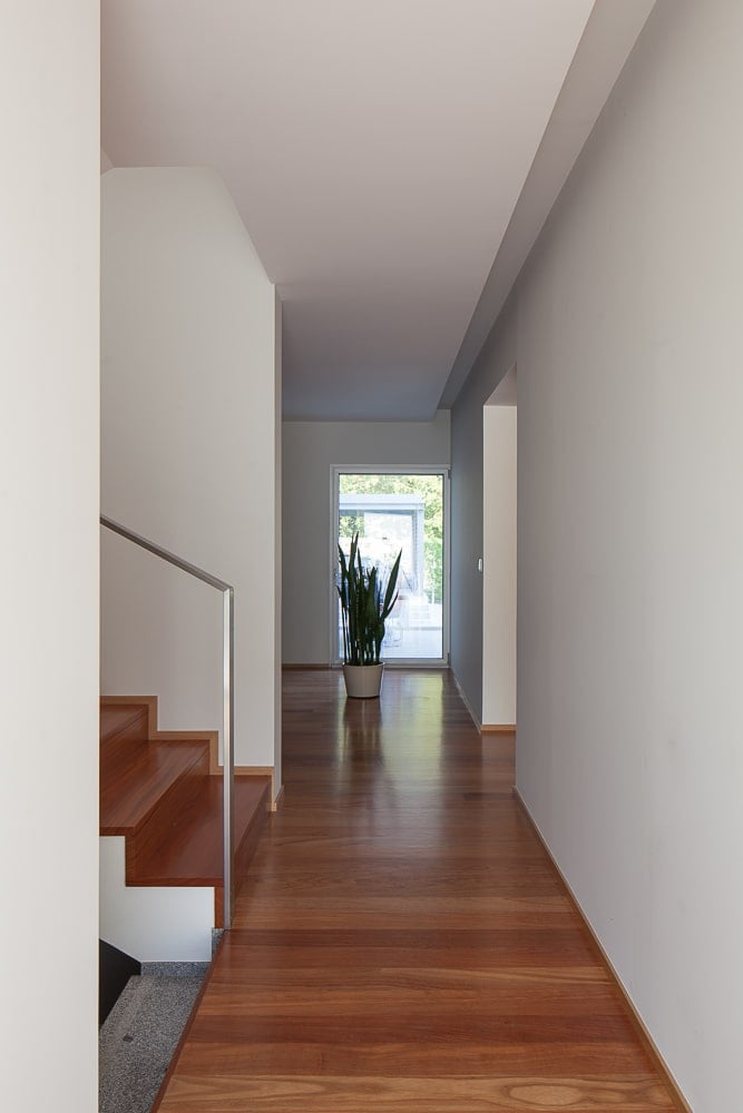 This is a hallway and landing for the staircase with hardwood flooring that match the steps of the staircase and it also has a potted plant on the far end.